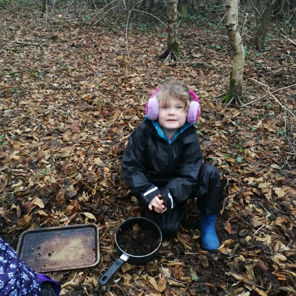 A young child in the forest making pretend food